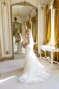 Bride standing in front of ornate mirror holding a bridal bouquet dressed in her beautiful bridal dress
