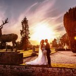 Wedding photographer captured a bride and groom at Gosfield Hall near a stag statue with a beautiful sun set
